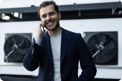 Chargé d'affaires souriant au téléphone devant des unités extérieures de climatisation industrielles, symbolisant l'interlocuteur unique pour un projet à Béziers.